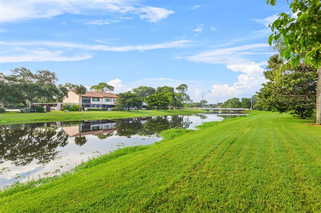 A grassy lawn slopes down to a calm pond reflecting a multi-story apartment building — 9669 86TH AVENUE UNIT 9669, SEMINOLE, FL