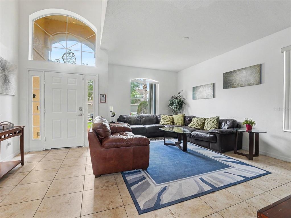 A living room with tile flooring, two brown sofas, a coffee table, and a front door — 4701 RUBY RED LANE, KISSIMMEE, FL