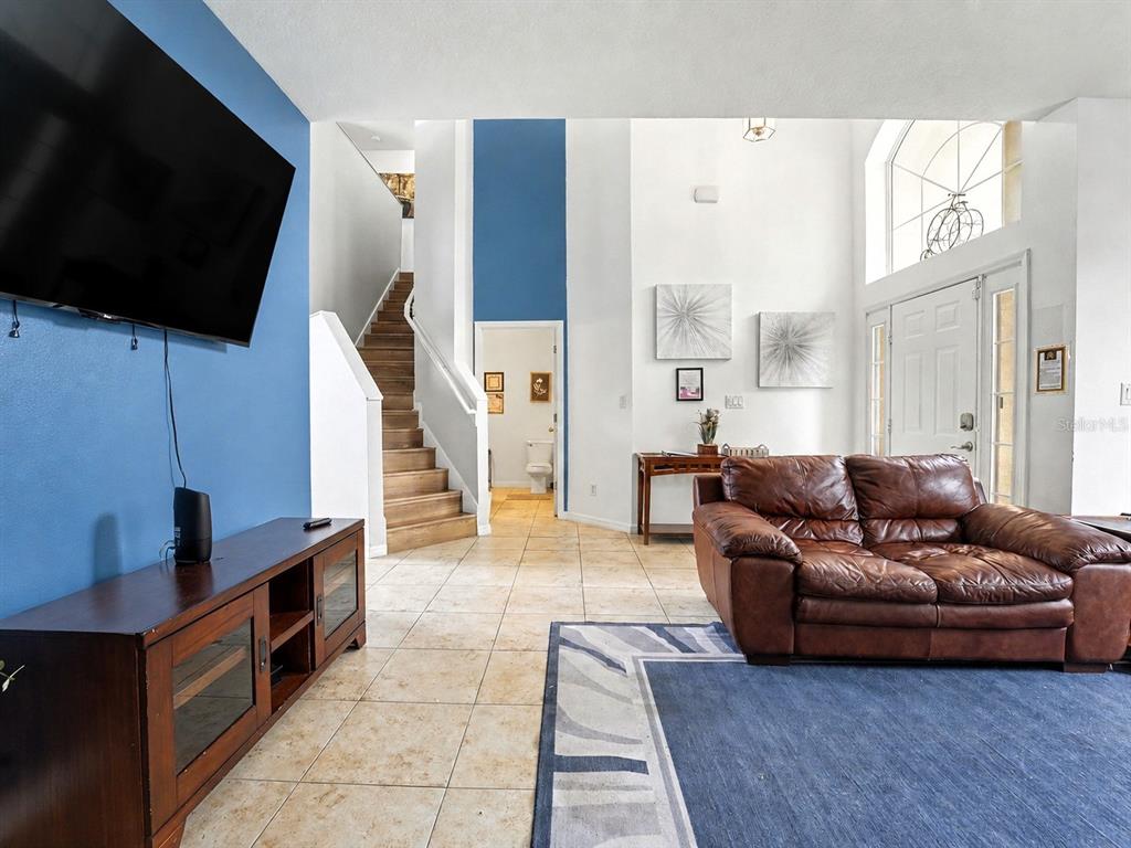A living room features a bright blue accent wall, tile flooring, and a staircase — 4701 RUBY RED LANE, KISSIMMEE, FL