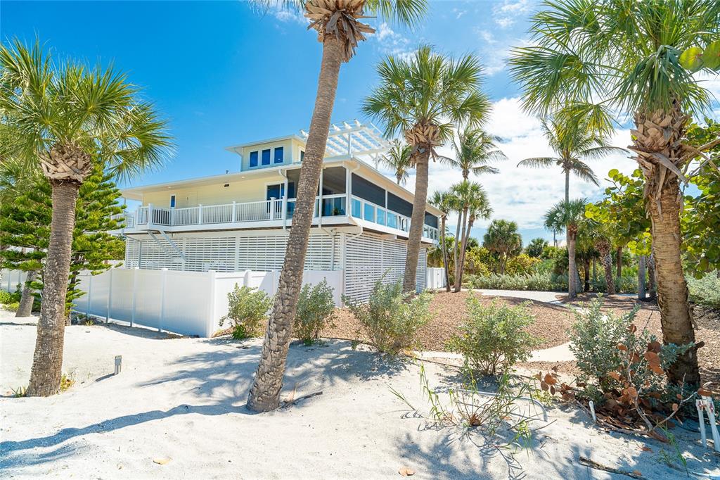 A yellow elevated house with a white fence and palm trees on a sandy lot — 230 N GULF BOULEVARD, PLACIDA, FL