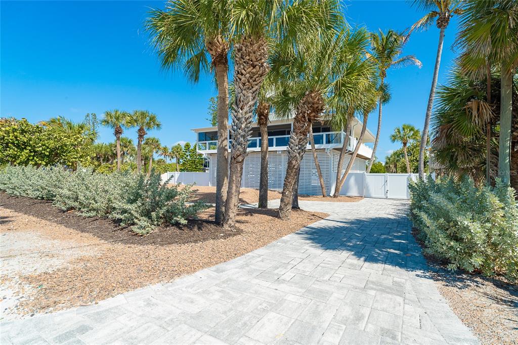 A paved driveway leads to a stilt house surrounded by palm trees and white fencing — 230 N GULF BOULEVARD, PLACIDA, FL