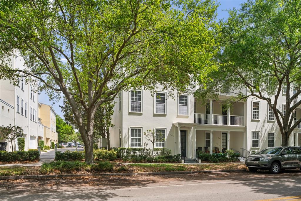A multi-story townhouse with a white facade, a front porch, and large trees in front — 1563 COMMON WAY ROAD, ORLANDO, FL