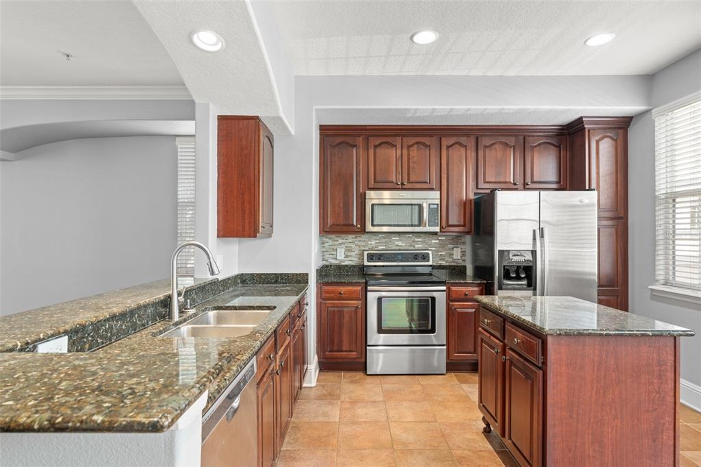 A kitchen with dark wood cabinets, granite countertops, stainless steel appliances, and a center island — 1563 COMMON WAY ROAD, ORLANDO, FL