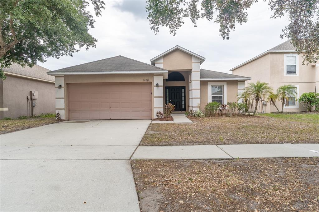 A single-story house with a beige stucco exterior, a two-car garage, and a covered entryway — 10917 BANYAN WOOD WAY, RIVERVIEW, FL
