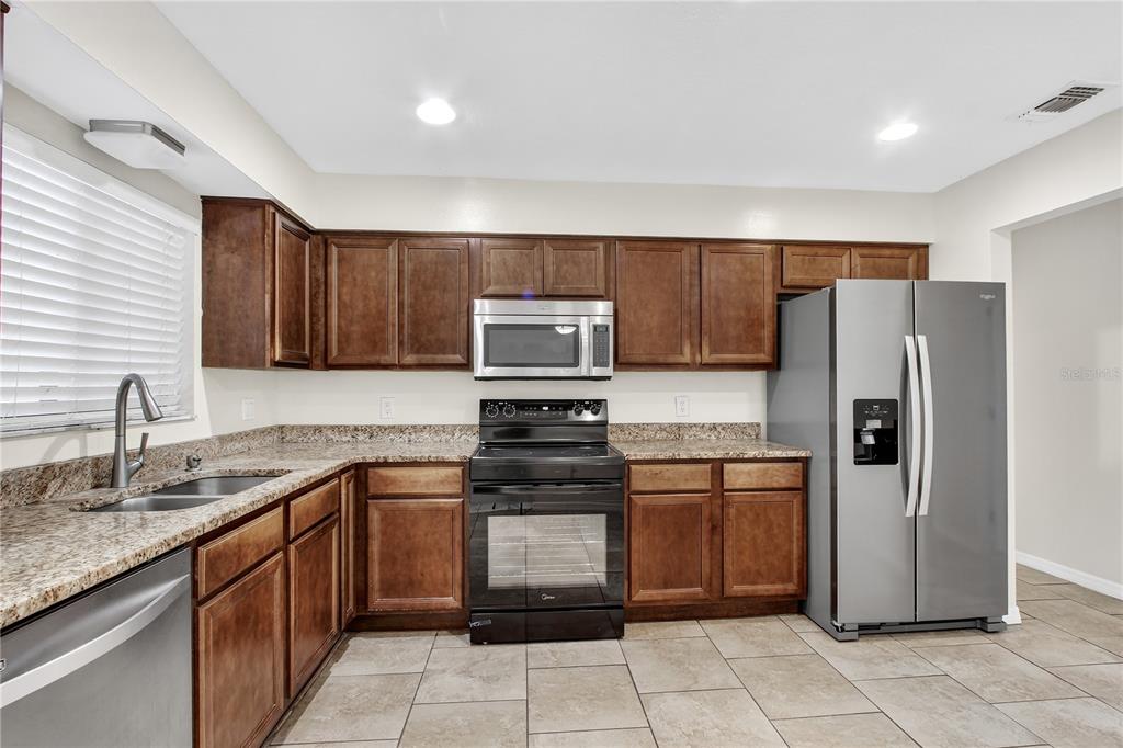 A kitchen with dark wood cabinets, granite countertops, stainless steel appliances, and tile flooring — 300 DUBLIN DRIVE, LAKE MARY, FL
