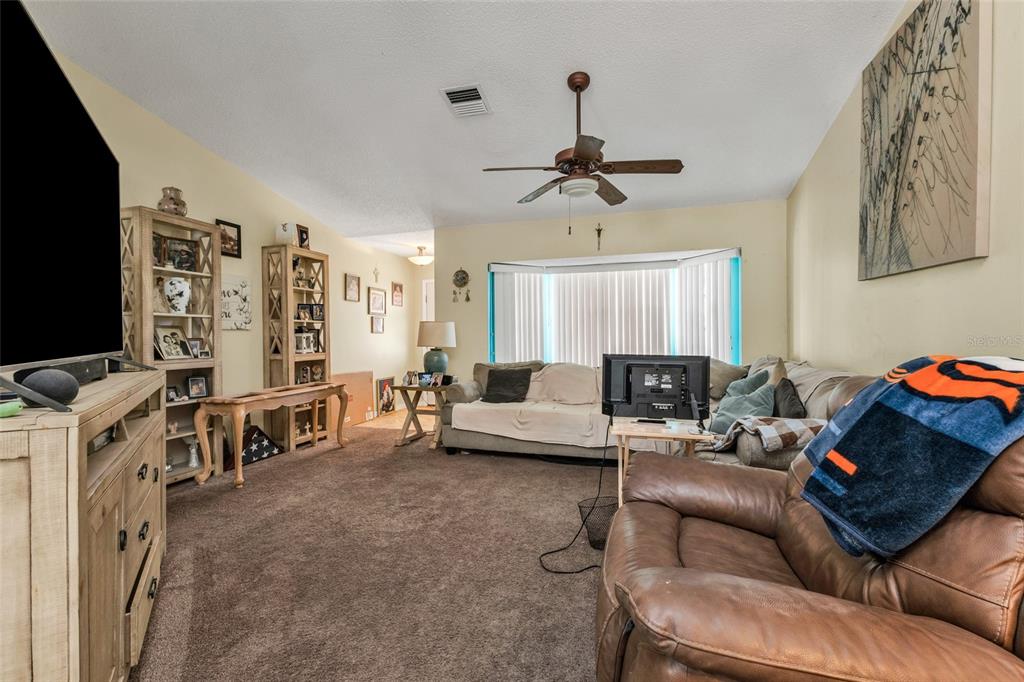 A living room features brown carpeting, a ceiling fan, a bay window, and wood furniture — 9261 STEUBENVILLE AVENUE, ENGLEWOOD, FL