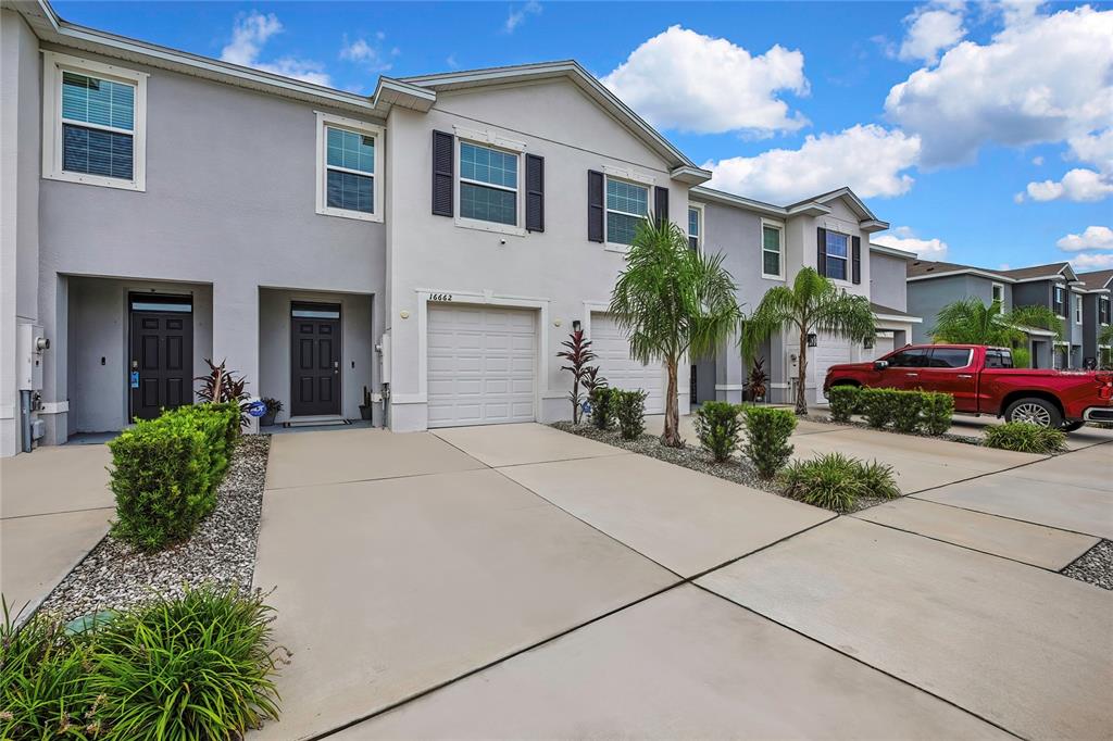 A row of two-story townhouses with attached garages and concrete driveways under a blue sky — 16662 MAUDE DRIVE, WIMAUMA, FL