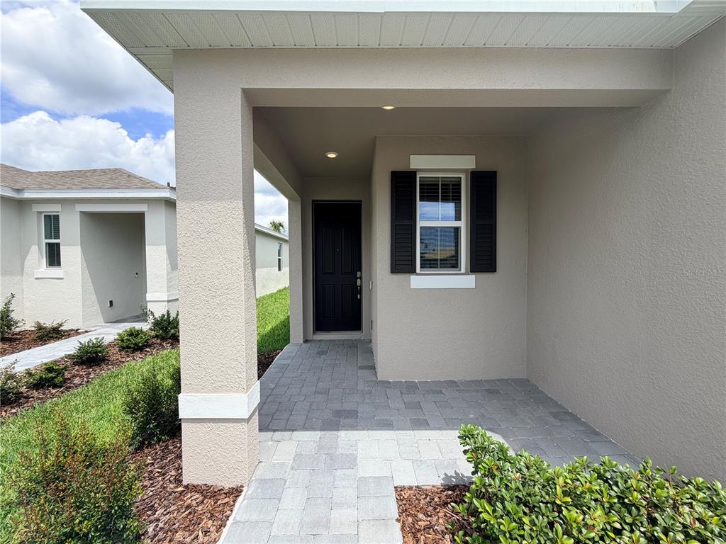 A covered entryway features a paved walkway, a dark front door, and a single window — 2029 ANTHEM DRIVE, ORANGE CITY, FL