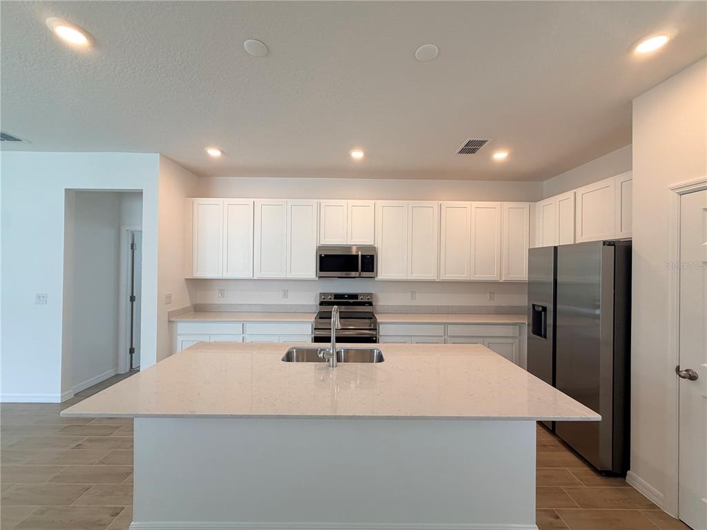 A modern kitchen features white cabinets, stainless steel appliances, and a large central island — 2029 ANTHEM DRIVE, ORANGE CITY, FL