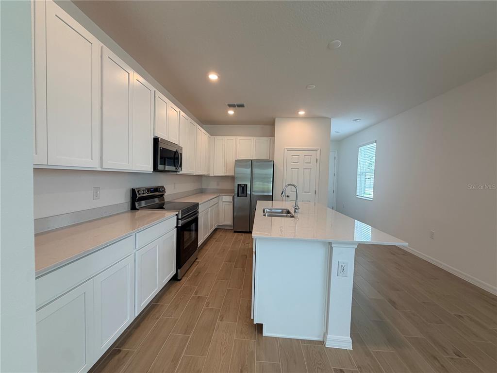 A modern kitchen features white cabinets, stainless steel appliances, a center island, and wood-look flooring — 2029 ANTHEM DRIVE, ORANGE CITY, FL