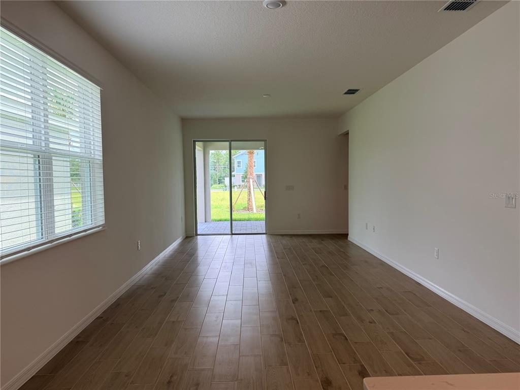 An empty living room features wood-look tile flooring, a large window, and sliding glass doors — 2029 ANTHEM DRIVE, ORANGE CITY, FL