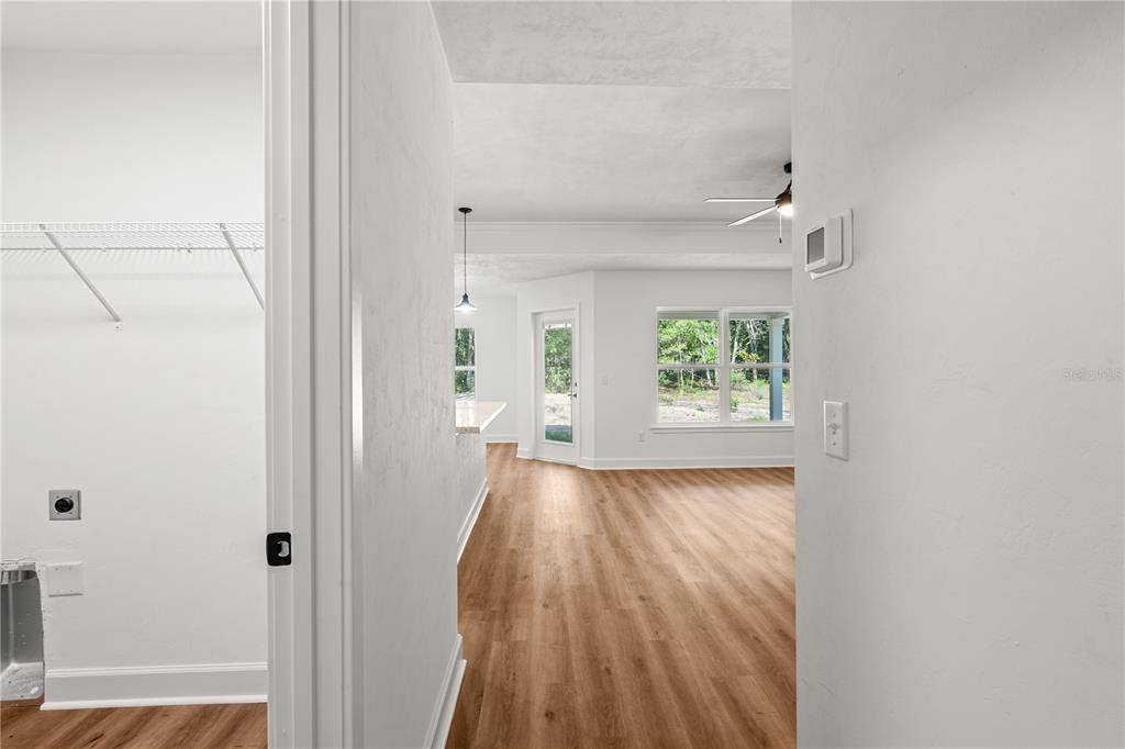 A hallway with wood-look flooring leads toward a doorway with natural light — 8030 NE 102ND COURT, BRONSON, FL