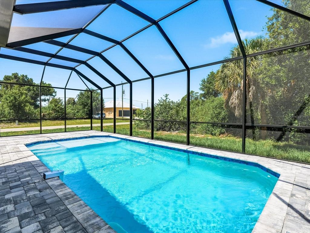 A rectangular swimming pool is enclosed by a black metal screen cage on a patio — 108 LOMAS RD, ROTONDA WEST, FL