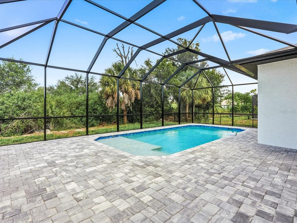 A screened-in patio features a rectangular swimming pool with a tanning ledge and paver flooring — 108 LOMAS RD, ROTONDA WEST, FL