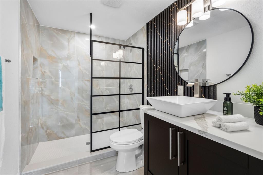 A modern bathroom features a walk-in shower, a vessel sink vanity, and a round mirror — 230 BEVERLY BOULEVARD, BRANDON, FL