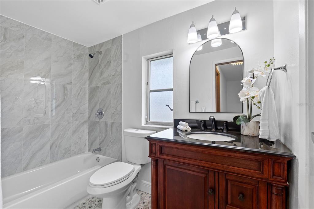 A bathroom features a marble-tiled shower, a wooden vanity with a black countertop, and a toilet — 230 BEVERLY BOULEVARD, BRANDON, FL