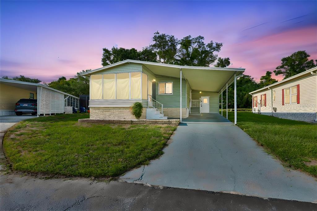 A light green manufactured home features a front sunroom, a carport, and a concrete driveway — 168 BEECHWOOD DRIVE UNIT 67, SAFETY HARBOR, FL