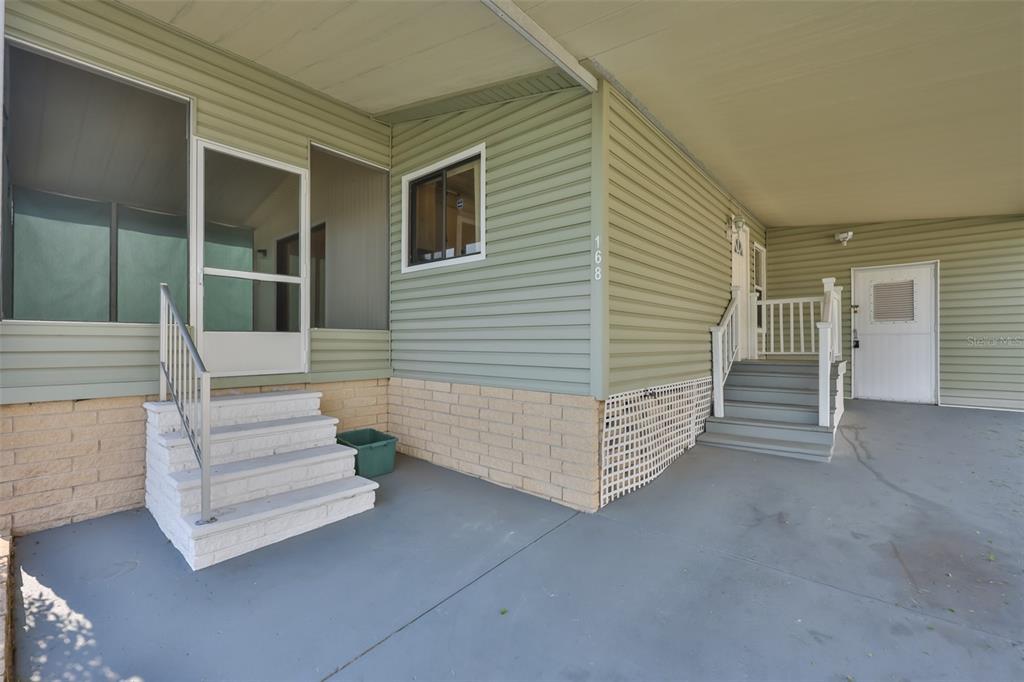 The exterior of a mobile home features light green siding, two sets of stairs, and a carport — 168 BEECHWOOD DRIVE UNIT 67, SAFETY HARBOR, FL
