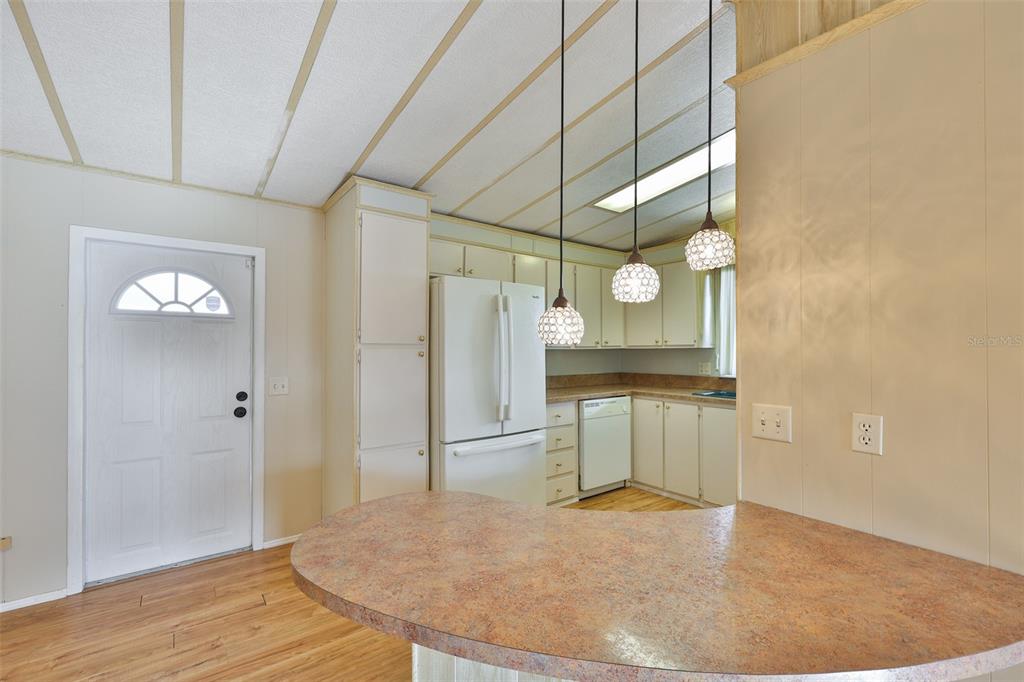 A kitchen features a curved peninsula, white appliances, pendant lighting, and light-colored wood-look flooring — 168 BEECHWOOD DRIVE UNIT 67, SAFETY HARBOR, FL