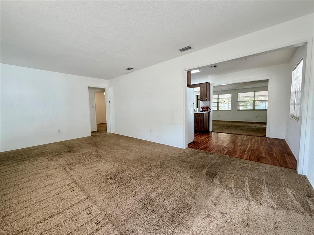 A living room with beige carpet leads into a kitchen and a carpeted dining area — 110 S CORONA AVENUE, CLEARWATER, FL