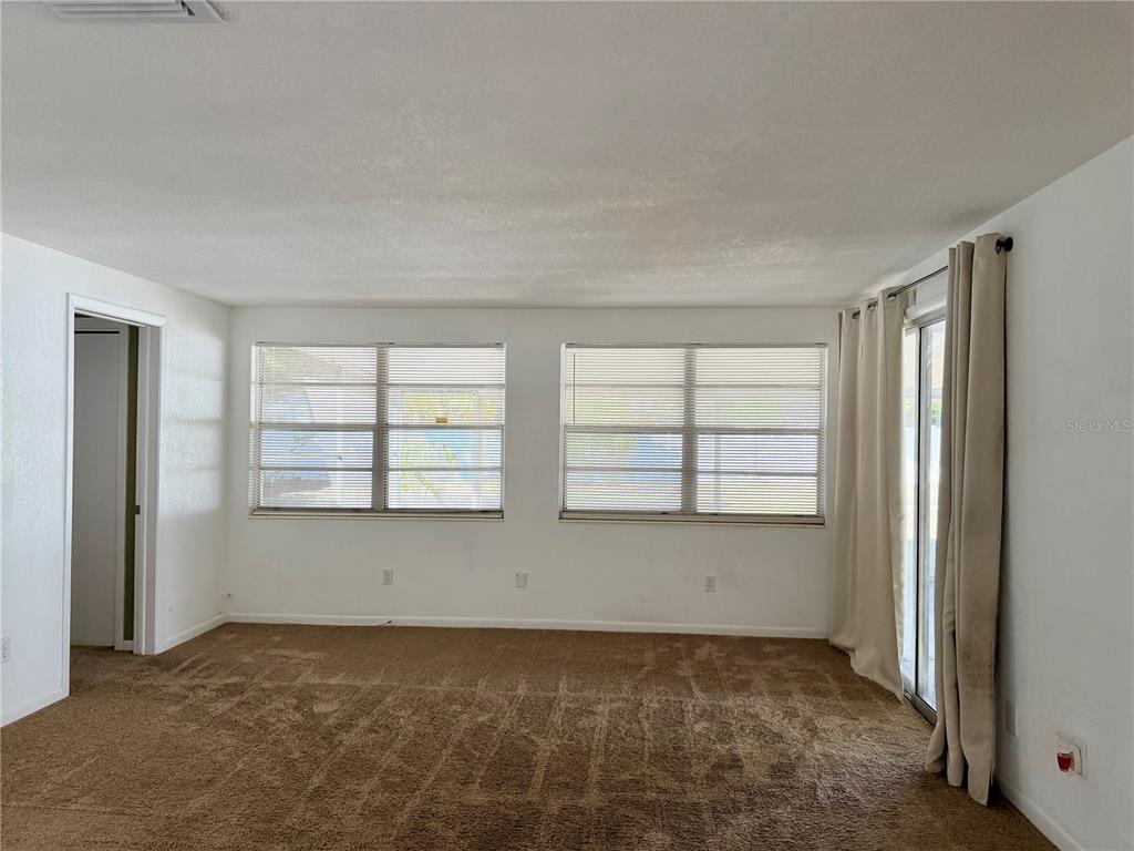 An empty room features brown carpeting, white walls, two windows with blinds, and sliding glass doors — 110 S CORONA AVENUE, CLEARWATER, FL