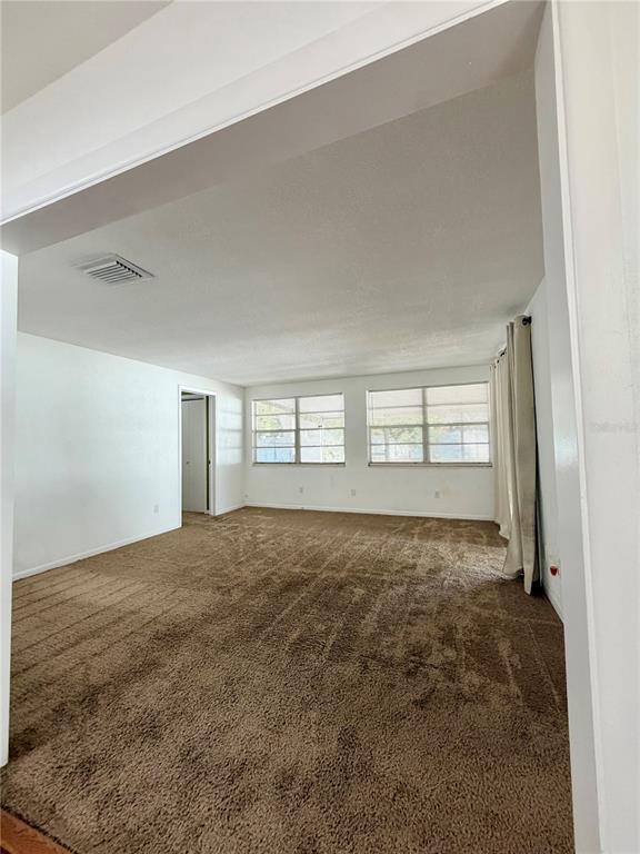 An empty living room features brown wall-to-wall carpeting, white walls, and two large windows — 110 S CORONA AVENUE, CLEARWATER, FL