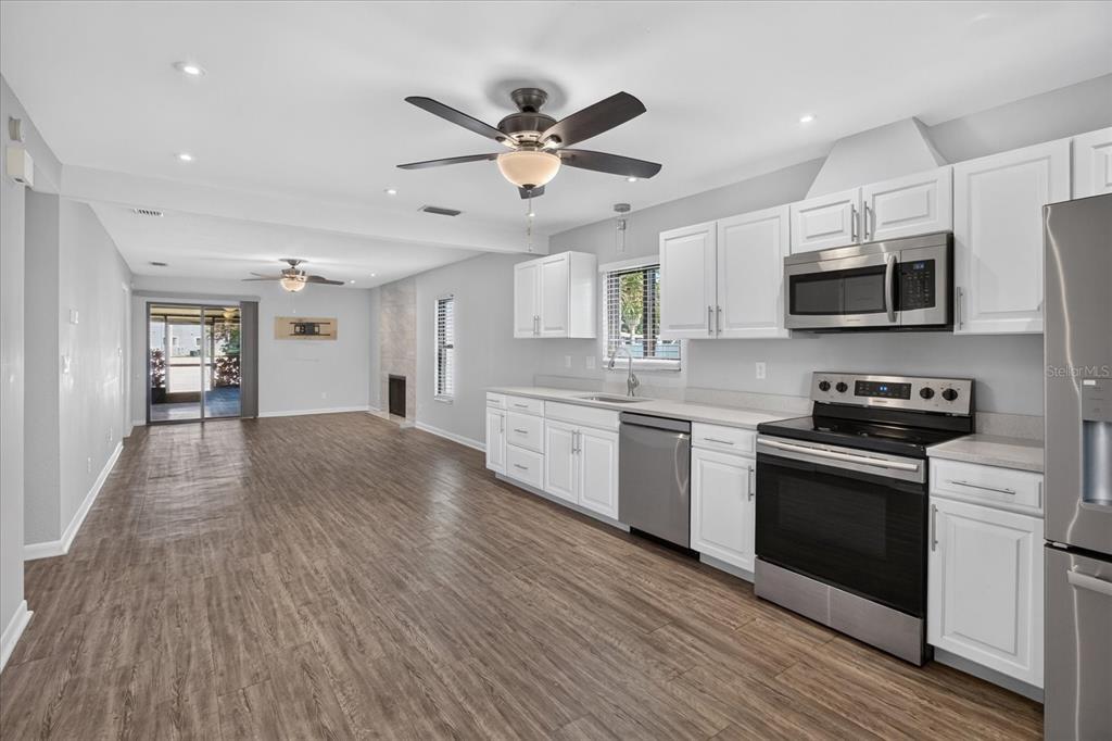 An open-concept kitchen and living area featuring white cabinets, stainless steel appliances, and wood flooring — 7360 ULMERTON ROAD UNIT 2E, LARGO, FL