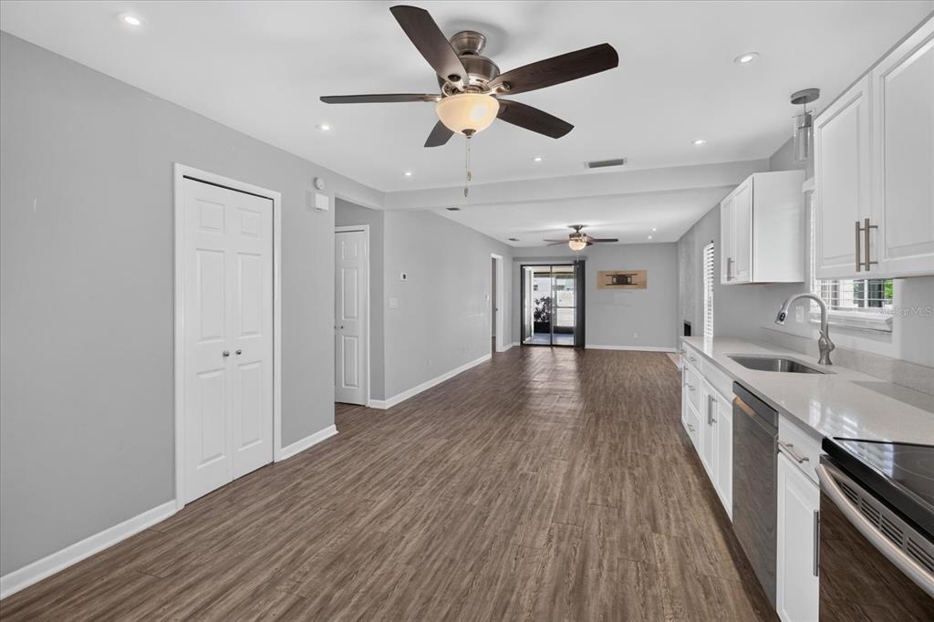 A kitchen with white cabinets and wood-look flooring opens into a living area with fans — 7360 ULMERTON ROAD UNIT 2E, LARGO, FL
