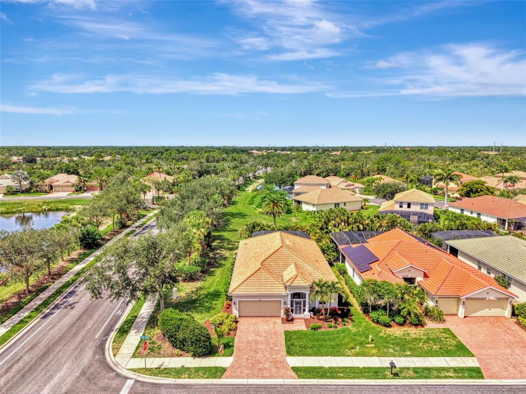 An aerial view shows a suburban neighborhood with houses, paved streets, and a small pond — 11783 PUMA PATH, VENICE, FL