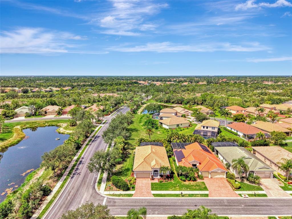An aerial view shows suburban houses with tiled roofs, a road, and a small pond — 11783 PUMA PATH, VENICE, FL