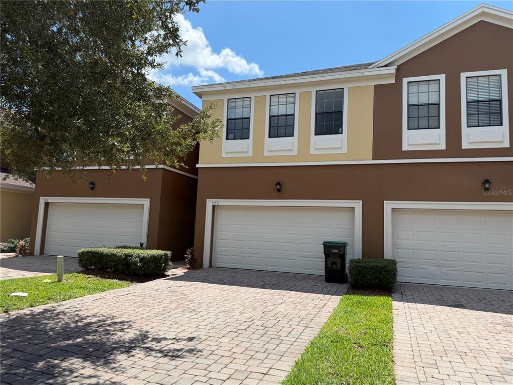 A row of townhouses with brown and yellow stucco exteriors, white garage doors, and paver driveways — 1550 PORTOFINO MEADOWS BOULEVARD, ORLANDO, FL