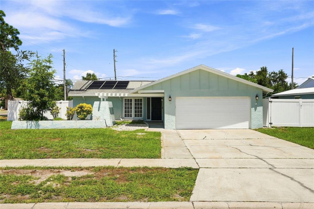A light green single-story house with a white garage door and solar panels on roof — 13691 SERENA DRIVE, LARGO, FL
