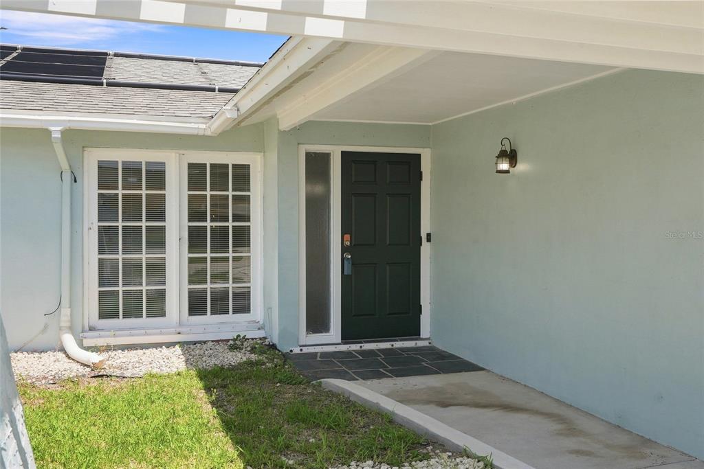 An exterior view of a house entrance with a dark door, windows, and a porch — 13691 SERENA DRIVE, LARGO, FL