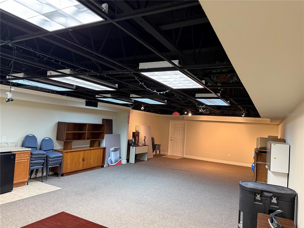 A large room with a black exposed ceiling, fluorescent lighting, and carpeted flooring — 221 W STATE ROAD 434, LONGWOOD, FL