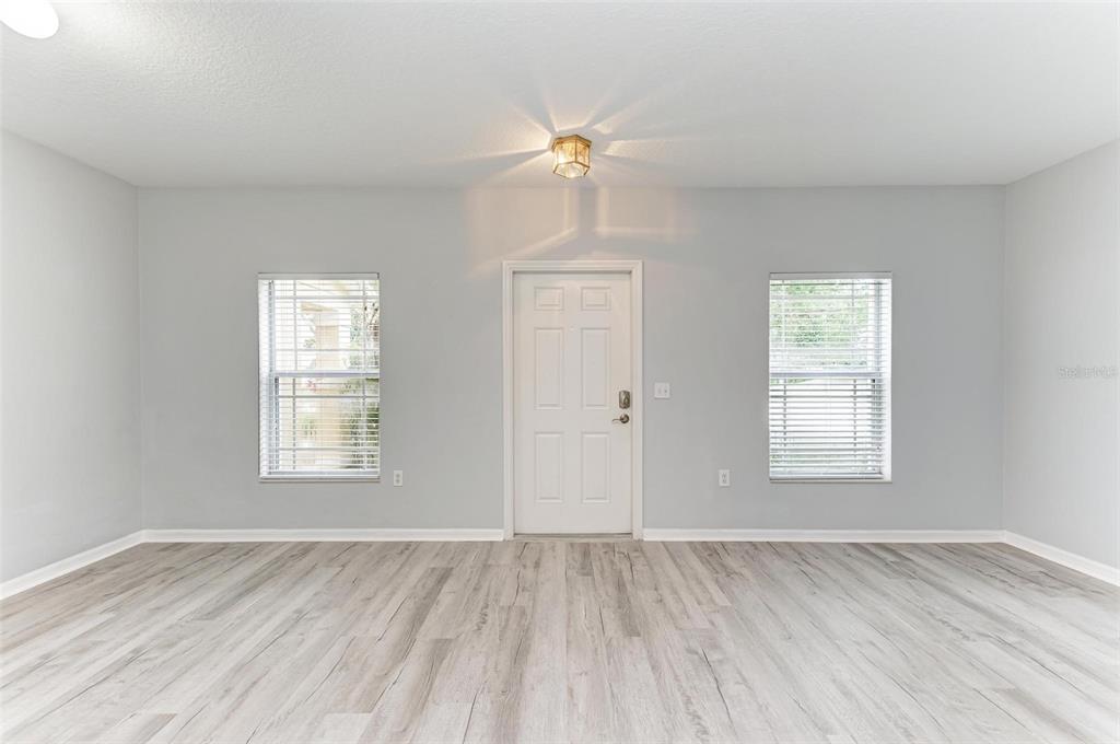 A bright, empty room features light gray walls, wood-look flooring, a central door, and two windows — 6218 FLAGFISH COURT UNIT 102, BRADENTON, FL