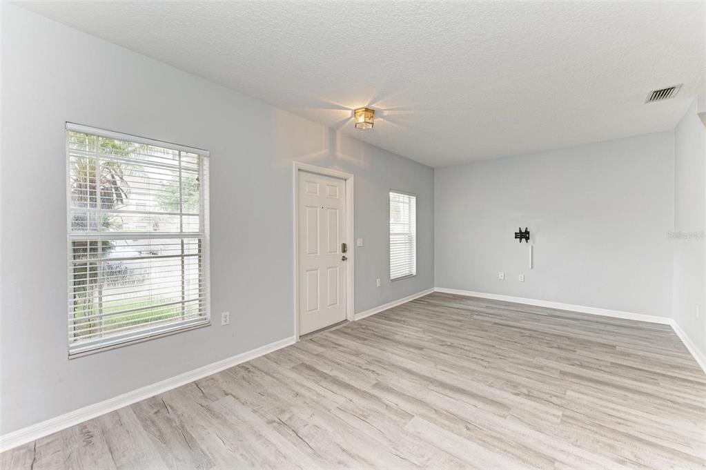 An empty room with light gray walls, wood-look flooring, a front door, and two windows — 6218 FLAGFISH COURT UNIT 102, BRADENTON, FL