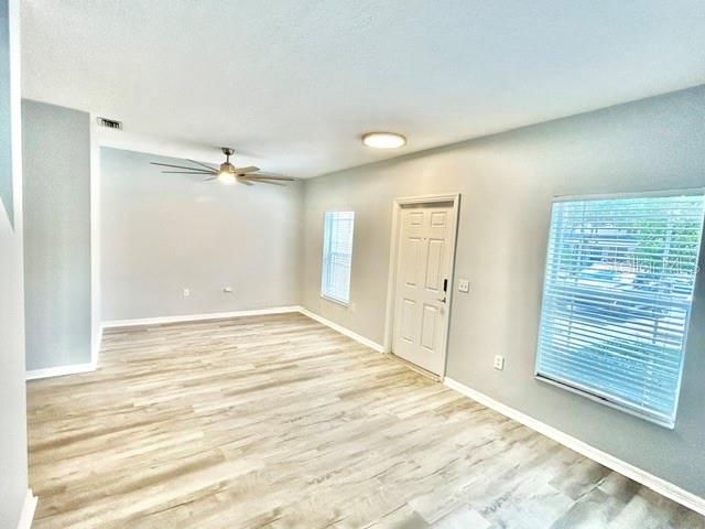 An empty room with light wood-look flooring, a ceiling fan, a white door, and windows — 6218 FLAGFISH COURT UNIT 102, BRADENTON, FL
