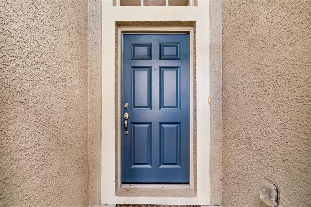 A blue front door with six panels is set within a beige stucco exterior wall — 211 FAIRMONT DRIVE, SPRING HILL, FL