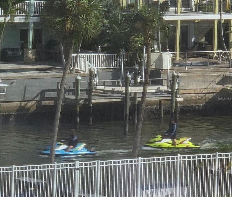Two people ride jet skis on a canal in front of a house with a dock — 4550 COVE CIRCLE UNIT 505, ST PETERSBURG, FL