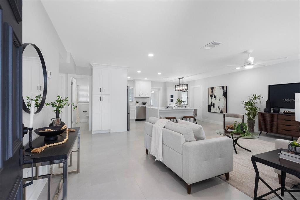 An open-concept living room and kitchen featuring white cabinetry, light tile floors, and modern furniture — 1601 HARDWOOD DRIVE, CLEARWATER, FL