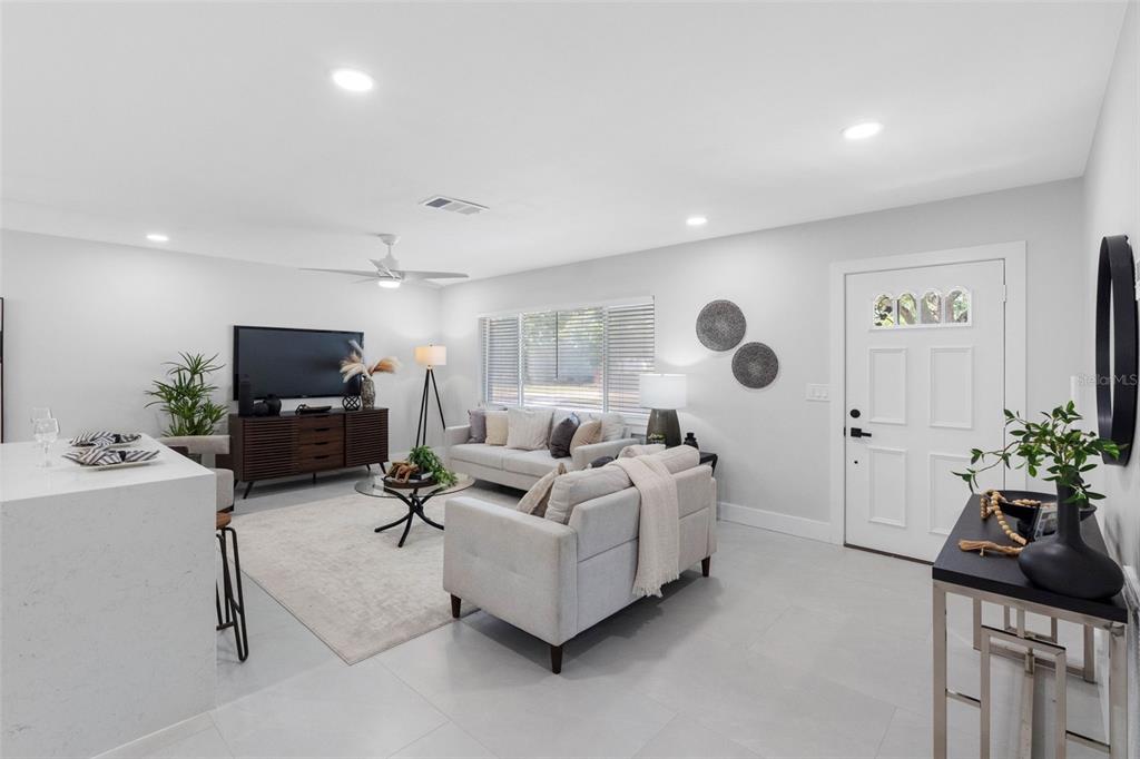 A bright living room features light gray tile flooring, two sofas, and a white front door — 1601 HARDWOOD DRIVE, CLEARWATER, FL