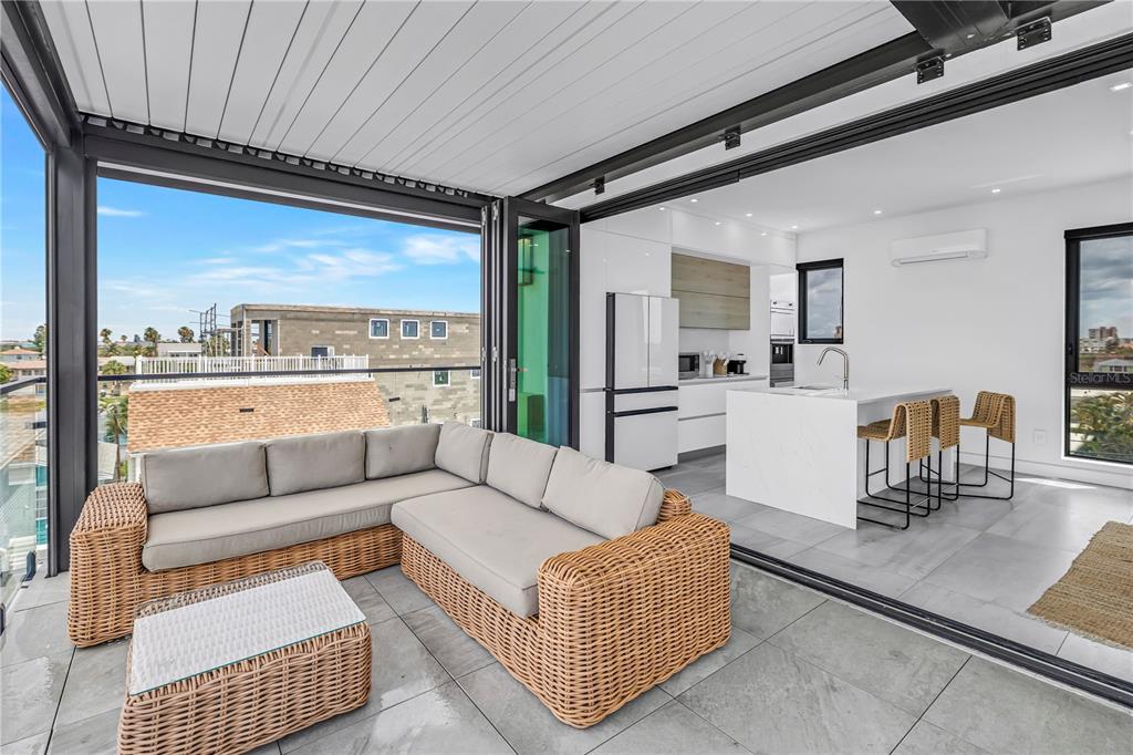 A modern indoor-outdoor living space features a wicker sectional, kitchen island, and folding glass doors — 30 80TH AVENUE, TREASURE ISLAND, FL