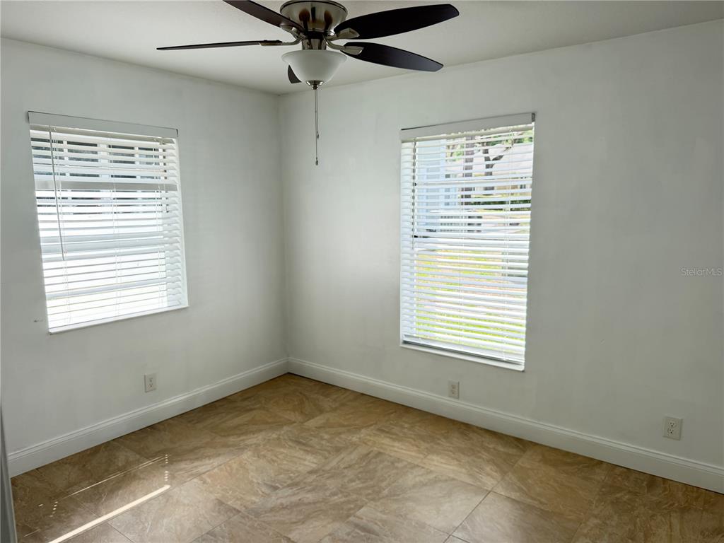 An empty bedroom features white walls, tile flooring, two windows with blinds, and a ceiling fan — 2564 SE 15TH AVENUE UNIT H, OCALA, FL