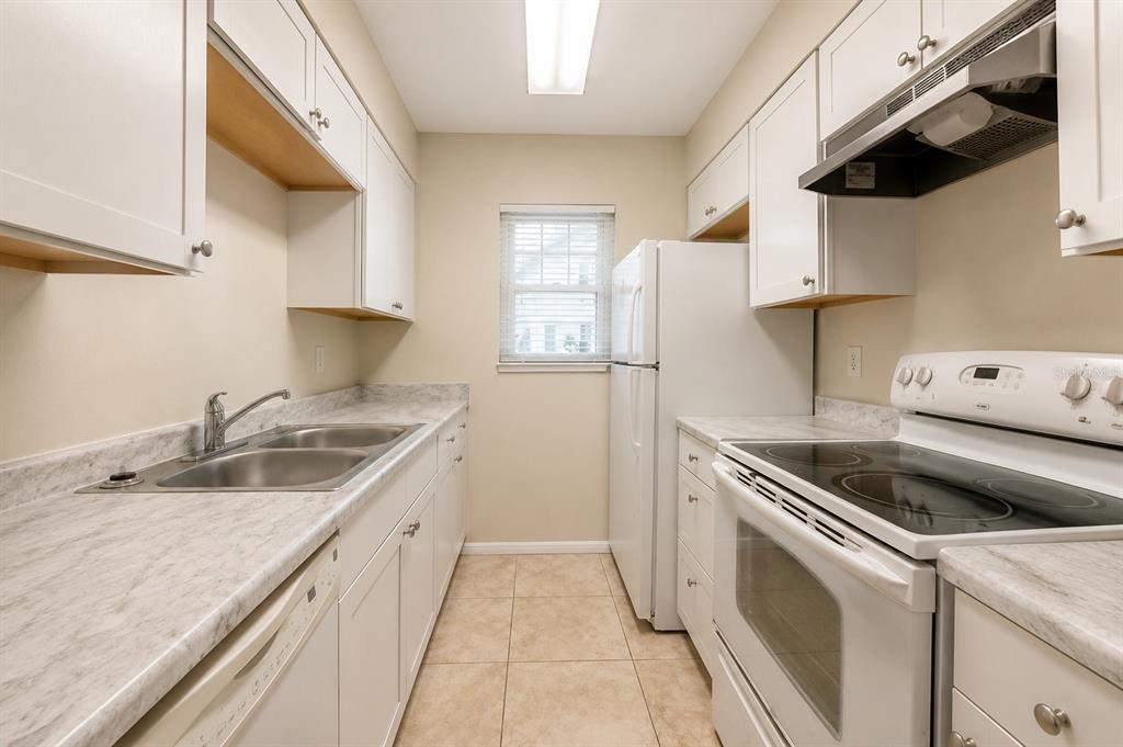 A galley kitchen features white cabinets, laminate countertops, a double sink, and white appliances — 828 SKY LAKE CIRCLE UNIT B, ORLANDO, FL