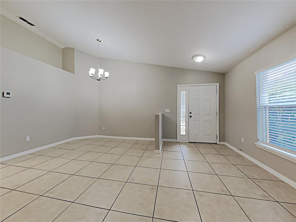 An empty dining room features beige tile flooring, a chandelier, and a front entry door — 511 WELLESLY STREET, OVIEDO, FL