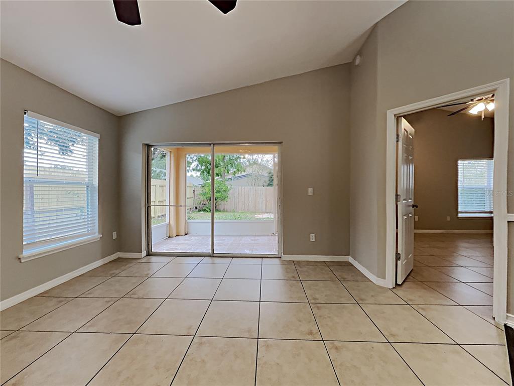 A room with beige tile flooring, a vaulted ceiling, sliding glass doors, and an open doorway — 511 WELLESLY STREET, OVIEDO, FL