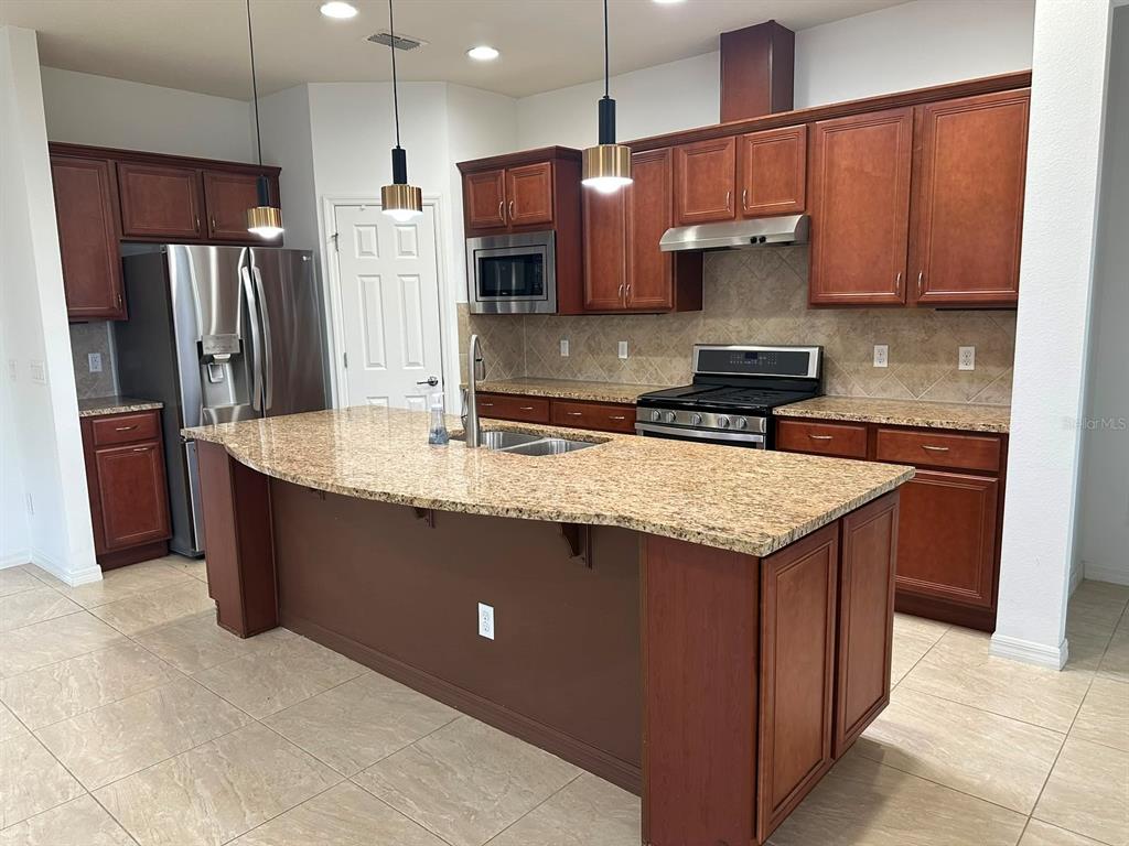 A kitchen features wood cabinets, granite countertops, a large island, and stainless steel appliances — 333 NAVARRA LANE, DAVENPORT, FL