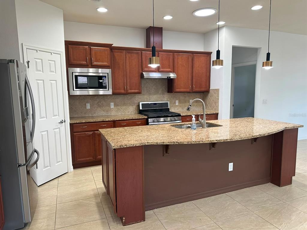 A kitchen features wood cabinets, granite countertops, a large island, and stainless steel appliances — 333 NAVARRA LANE, DAVENPORT, FL