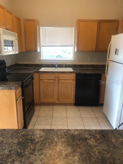 A kitchen features light wood cabinets, a white refrigerator, a black dishwasher, and tiled flooring — 10961 BURNT MILL ROAD UNIT 1518, JACKSONVILLE, FL