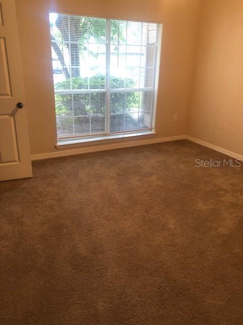 An empty bedroom features beige carpet, tan walls, and a large window with white blinds — 10961 BURNT MILL ROAD UNIT 1518, JACKSONVILLE, FL